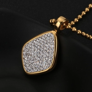 Détail d'un pendentif goutte dorée orné de strass brillants sur une chaîne à billes