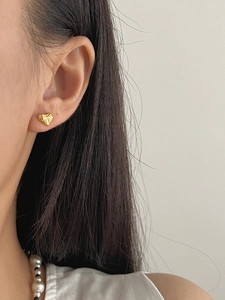 Detail view of heart-shaped gold stud earring with delicate radial texture on model