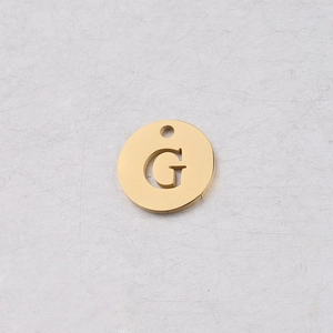 Gros plan d'un pendentif rond de 12mm en acier doré avec une lettre G évidée au centre
