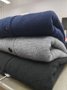 Detail view of stacked knit cardigans in navy blue, light grey, and black with button details