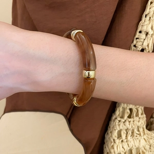 Detail of amber acrylic segment bracelet with gold metal rings on a model's wrist
