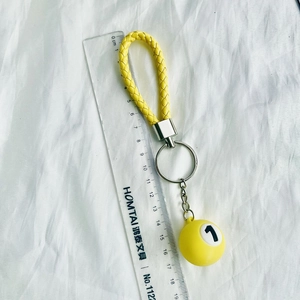 Close-up of a mini yellow billiard ball keychain with a braided strap next to a ruler