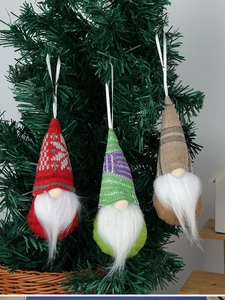 Nahaufnahme von drei gestrickten Weihnachtswichteln an einem grünen Tannenzweig