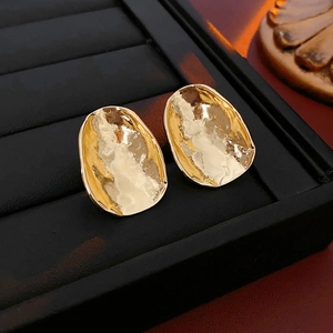 Macro detail of gold oval stud earrings with irregular hammered metal texture in a black tray