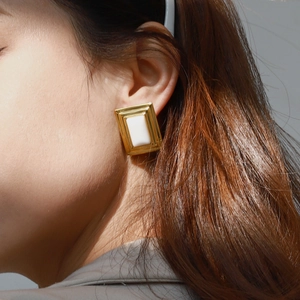 Minimalist geometric gold earrings with white rectangular inlay worn by a model