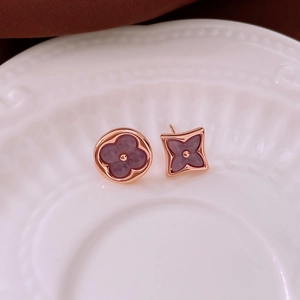 Detail of asymmetrical rose gold studs with purple floral motifs on a ceramic dish