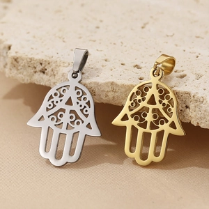 Close-up of gold and silver hollow Hamsa Hand pendants on a beige stone surface