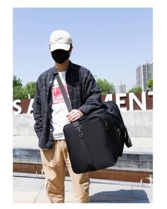 Black Oxford cloth travel bag with adjustable strap worn by a male model outdoors