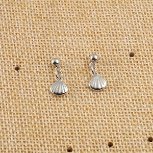 Détail de boucles d'oreilles argentées en forme de coquillage sur fond de rotin tressé