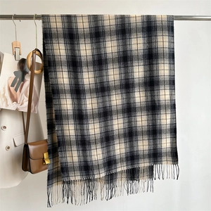 Detailed view of beige and black plaid scarf with fringe texture on metal hanger