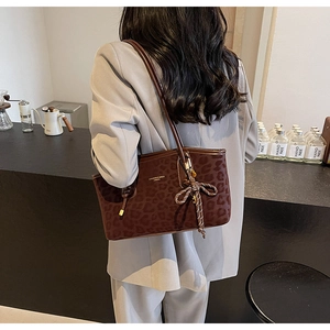 Détail du sac cabas léopard avec breloque nœud tressé et fines lanières dans un café