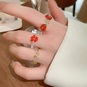 Close-up of colorful beaded flower rings on fingers with red and green glass beads