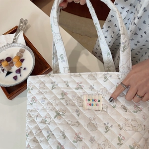 Close-up of white quilted tote bag with floral rabbit pattern and fabric brand label