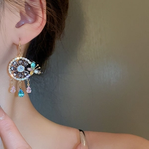 Close-up of gold tassel earrings with colorful zircons, flower petals and butterfly detail
