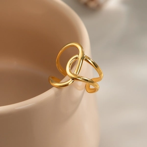 Bague ouverte dorée géométrique présentée sur le bord d'une tasse en céramique