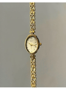 Détail d'une montre ovale dorée avec chiffres romains et bracelet en chaîne chic