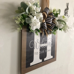 Detail of wooden welcome sign with letter H, white faux flowers and burlap bow decor