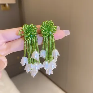 Macro shot of lily of the valley earrings with green beads and white bell-shaped petals