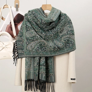 Detail of green paisley pashmina scarf with black tassels over a beige coat