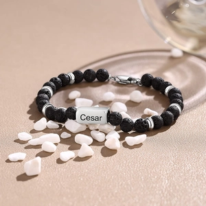 Detailed shot of lava stone bracelet with personalized engraved steel tag on sand background