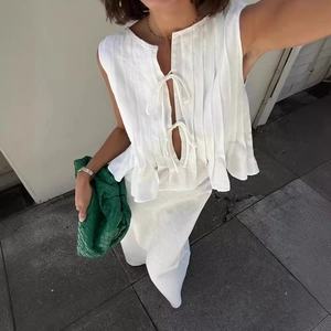White linen sleeveless pleated top and skirt set with green woven leather bag accessory