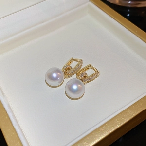 Vue macro de boucles d'oreilles géométriques dorées avec zircons et perles blanches