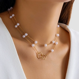 Detail of layered gold necklace with imitation pearls and double ring pendant on model