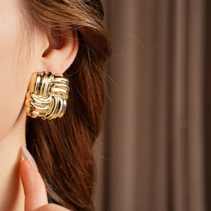Close-up of a model wearing golden square knot earrings with textured metallic finish
