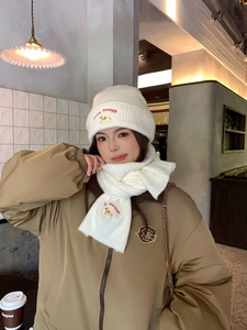 Close-up of white knitted hat and scarf set with red puppy embroidery in a cafe