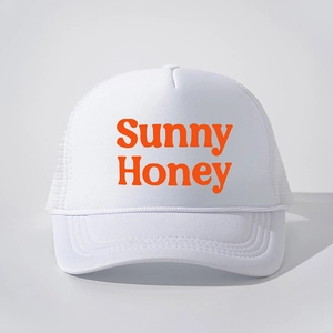 Detailed close-up of white trucker hat featuring orange Sunny Honey print and mesh back