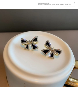 Detailed close-up of S925 gold bow earrings with black finish and sparkling rhinestones