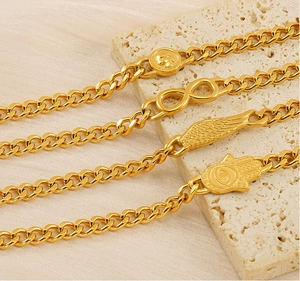 Dettaglio di quattro bracciali a catena cubana dorati con ciondoli teschio, infinito e ali