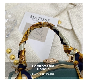 Detail of dark green handbag featuring a silk scarf-wrapped handle and golden lock clasp