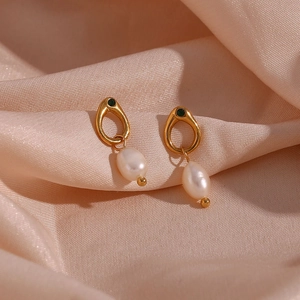Detail of vintage gold earrings with drop pearl and green gemstone on silk