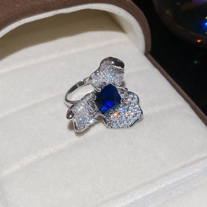 Détail macro d'une bague argentée avec gemme bleue carrée et sertissage floral en zircon