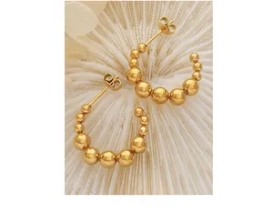 Vue macro de boucles d'oreilles créoles dorées à perles sur fond corail blanc