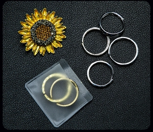 Close-up of golden sunflower pendant and assorted silver metal rings on black leather