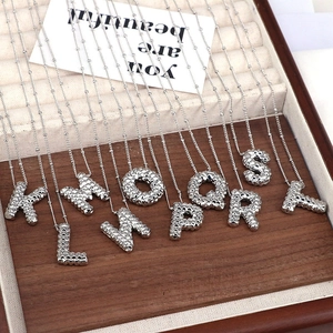 Detail of silver letter pendants with rivet texture in a wooden jewelry display box