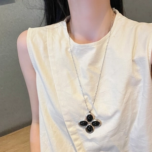 Close-up of a silver long necklace featuring a vintage black four-leaf clover pendant