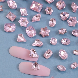 Close-up of pink crystal nail art rhinestones in various shapes with manicure samples