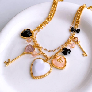 Dettaglio di ciondoli vintage a cuore e chiave su una collana dorata a strati