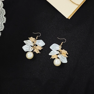 Detailed view of white petal earrings with pearls on a vintage black fabric background