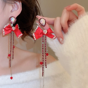 Close-up of red ribbon bow earrings with rhinestone tassels and heart-shaped crystal