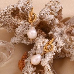 Detail of 18K gold knot stud earrings with baroque pearls on a white coral base
