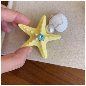 Detail of yellow starfish hair clip with blue crystal star, pearl and seashell accents