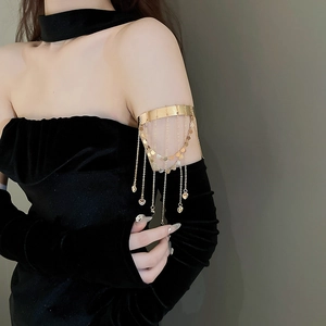 Macro detail of gold arm cuff with dangling chain tassels and heart pendants