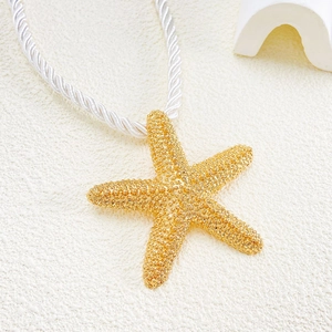 Macro shot of gold starfish pendant with grain texture on white braided rope necklace