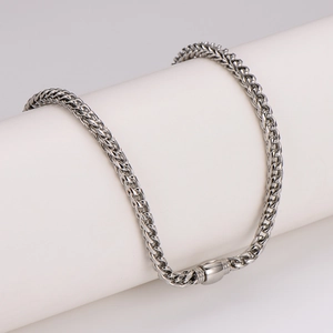 Minimalist silver stainless steel woven wheat chain necklace on a white pedestal display