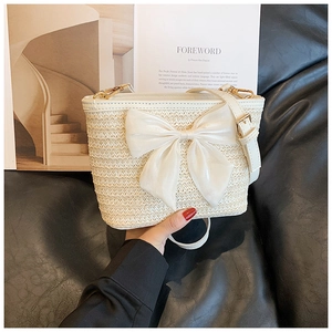 Detail of woven straw bucket bag with large white satin bow and gold metal hardware