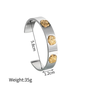 Detail view of 1.2cm wide C-shaped stainless steel cuff with golden floral embossed accents